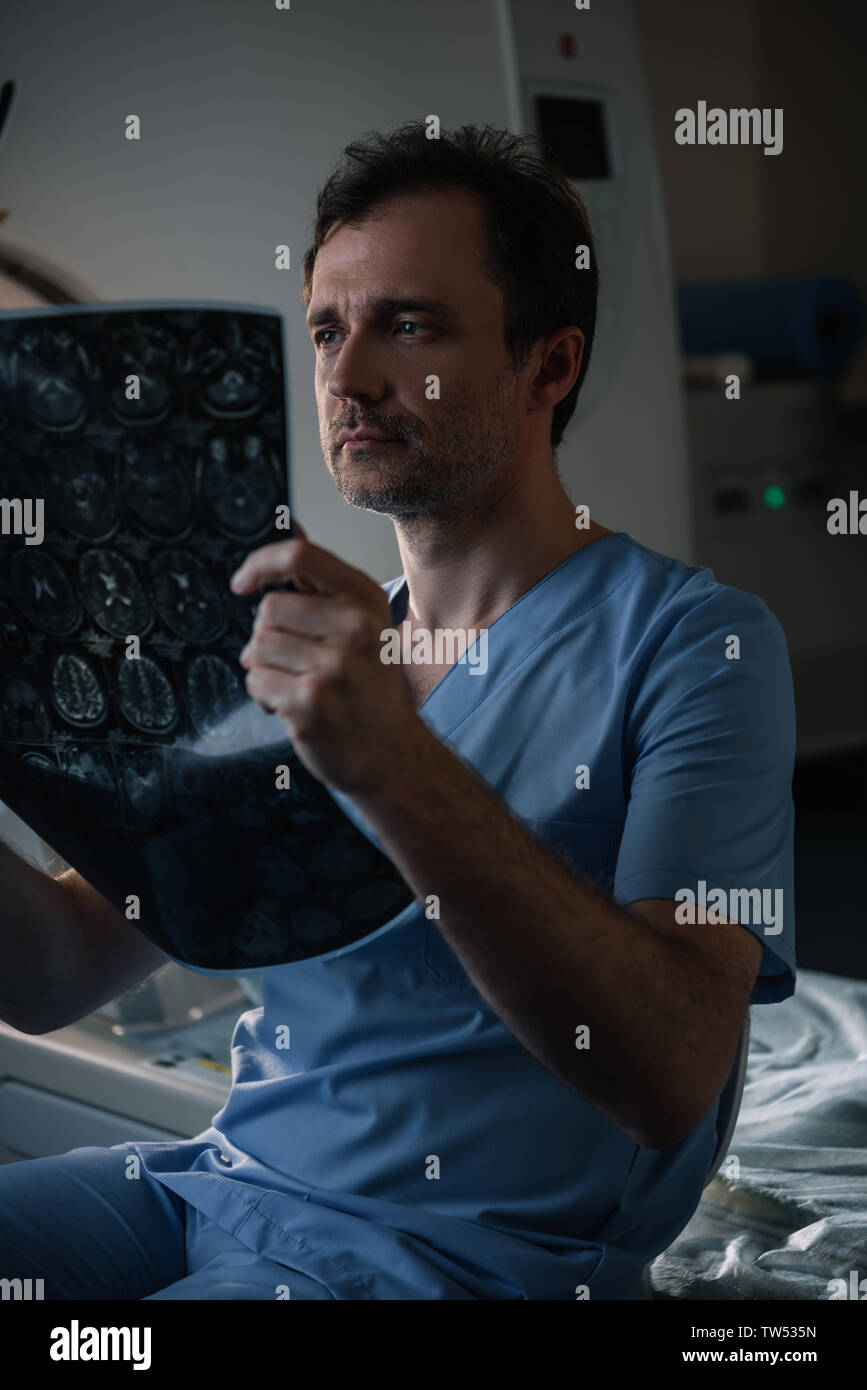 Serious doctor examining x-ray diagnostic alors qu'il était assis près de scanner à l'hôpital Banque D'Images