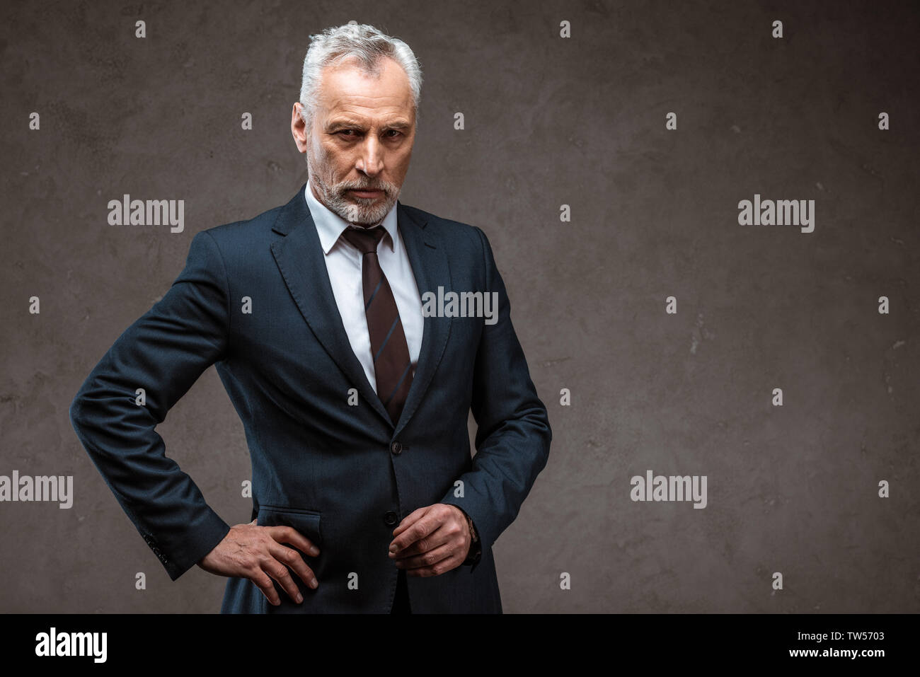 Confident businessman in suit standing with hand on hip sur gris Banque D'Images