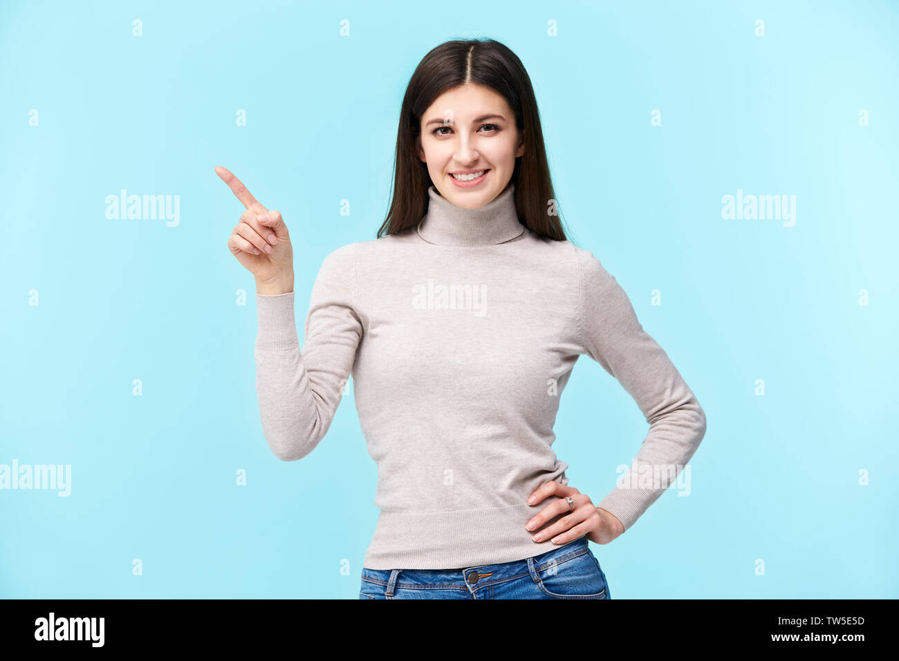 Portrait d'une belle jeune femme de race blanche, de pointer du doigt quelque chose, smiling, isolé sur fond bleu Banque D'Images