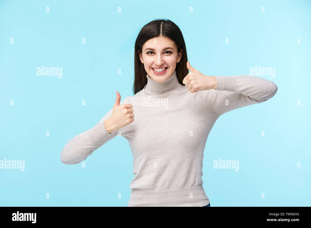 Portrait d'une belle jeune femme de race blanche avec deux Thumbs up, looking at camera smiling, isolé sur fond bleu Banque D'Images