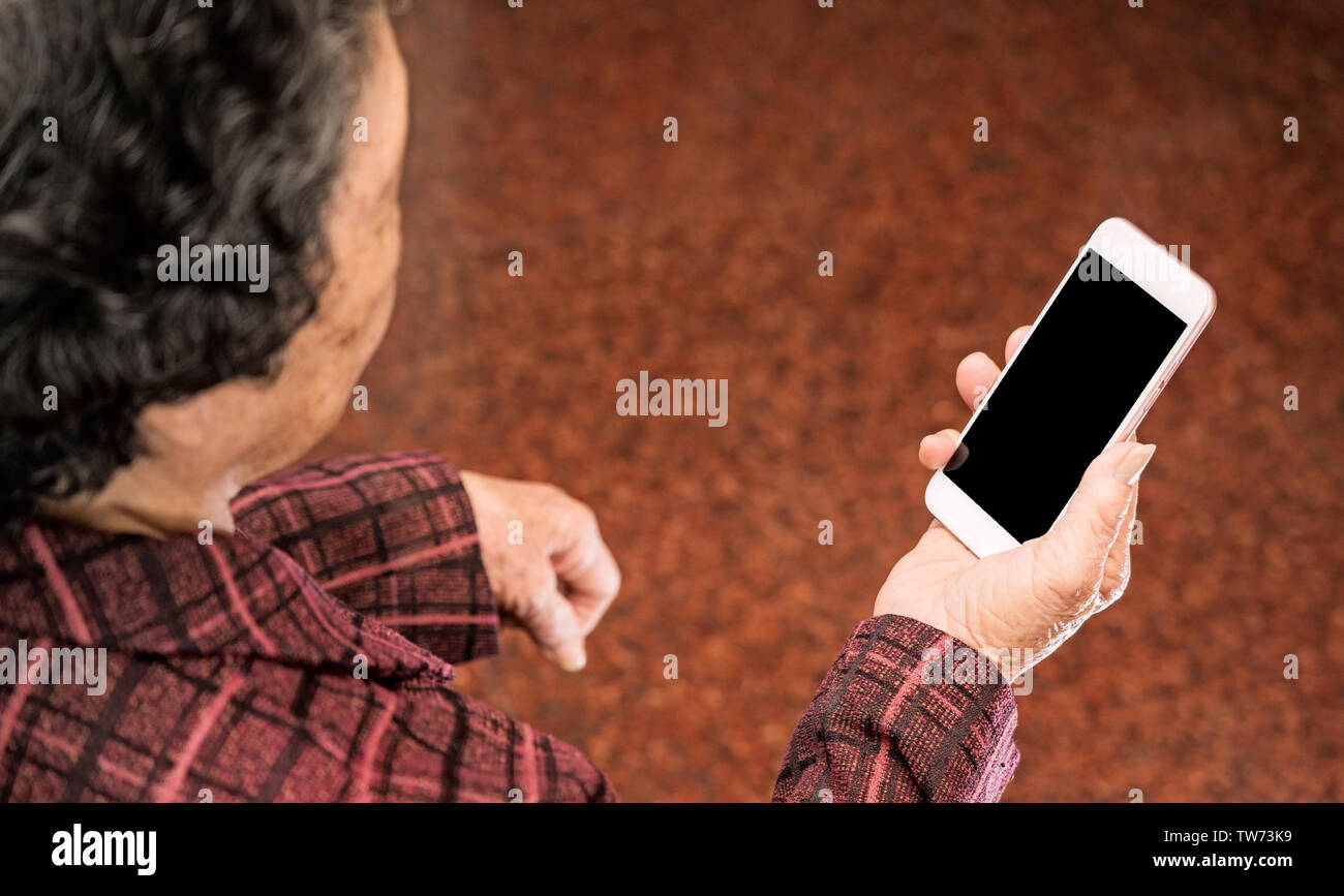 Vieille Femme Asiatique assis et regarder à travers quelque chose sur smartphone moderne, faisant la liaison avec d'autres personnes à la maison, un salon de la technologie, Close up Banque D'Images