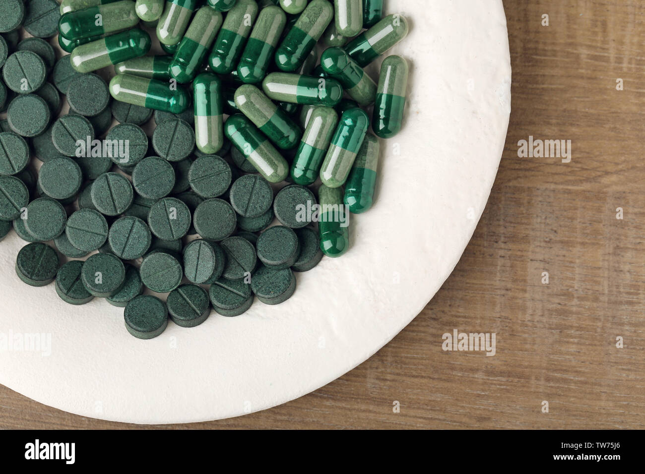 La plaque avec des capsules et des comprimés de spiruline sur table Banque D'Images