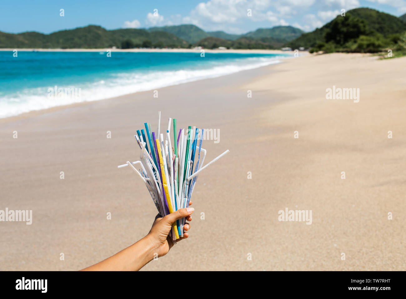 Main tenant tas de pailles en plastique utilisés sur fond de plage propre et vagues de l'océan. La pollution des océans de plastique, crise de l'environnement. Dire non en plastique. Banque D'Images