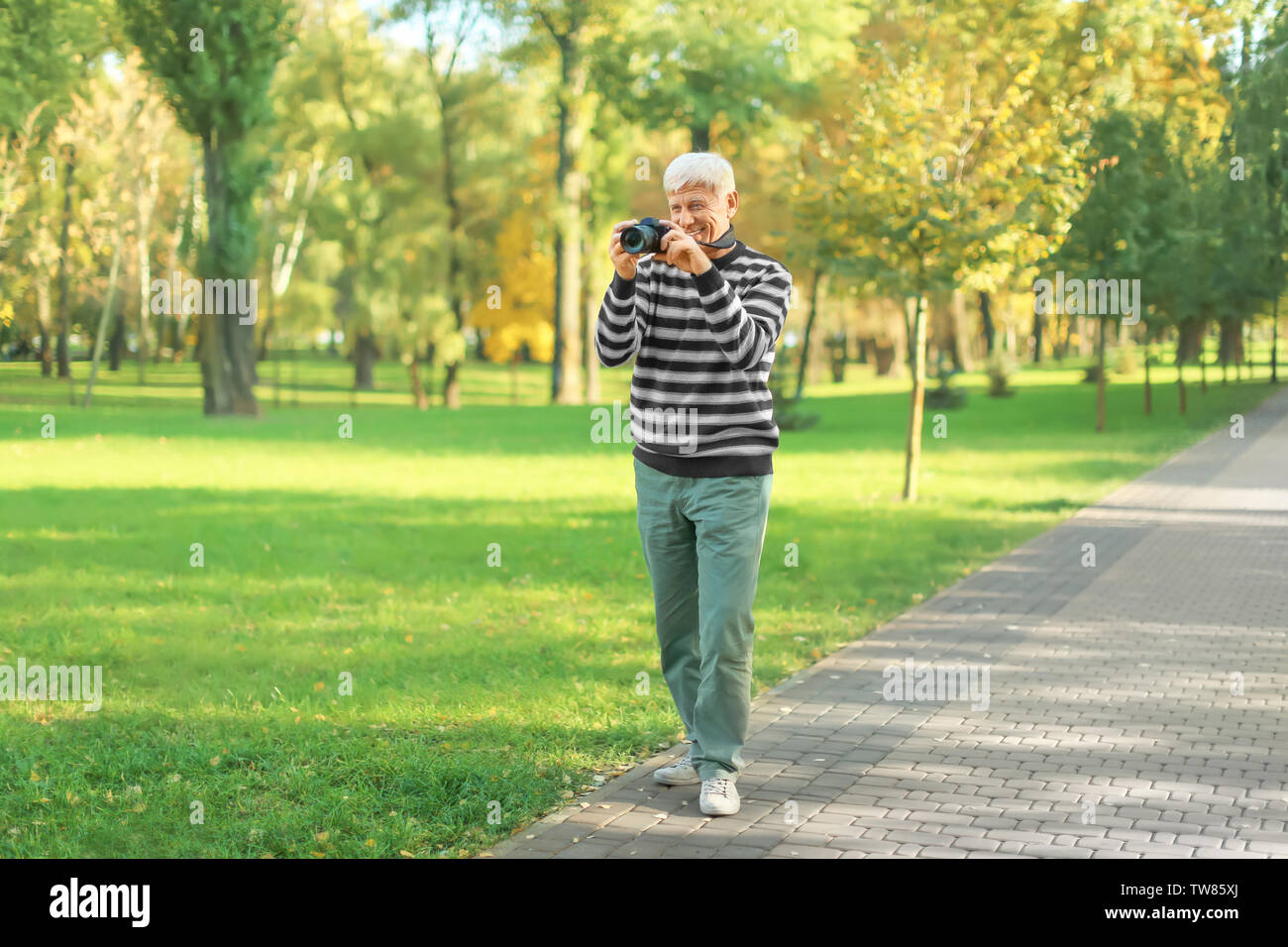 Homme mûr élégant taking photo in autumn park Banque D'Images