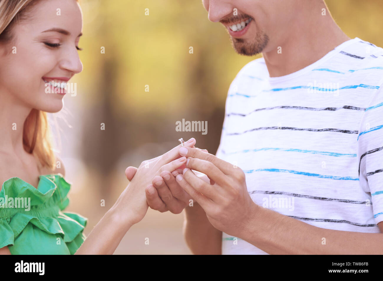 Young man putting bague de fiançailles sur fiancee's finger in park Banque D'Images