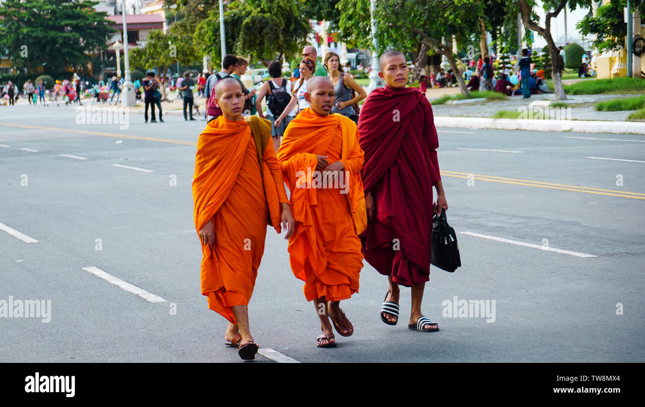 Phnom Penh, Cambodge - Août 2016 : jeunes moines en robe orange distinctive en marchant dans la rue en face d'un groupe de touristes. Banque D'Images