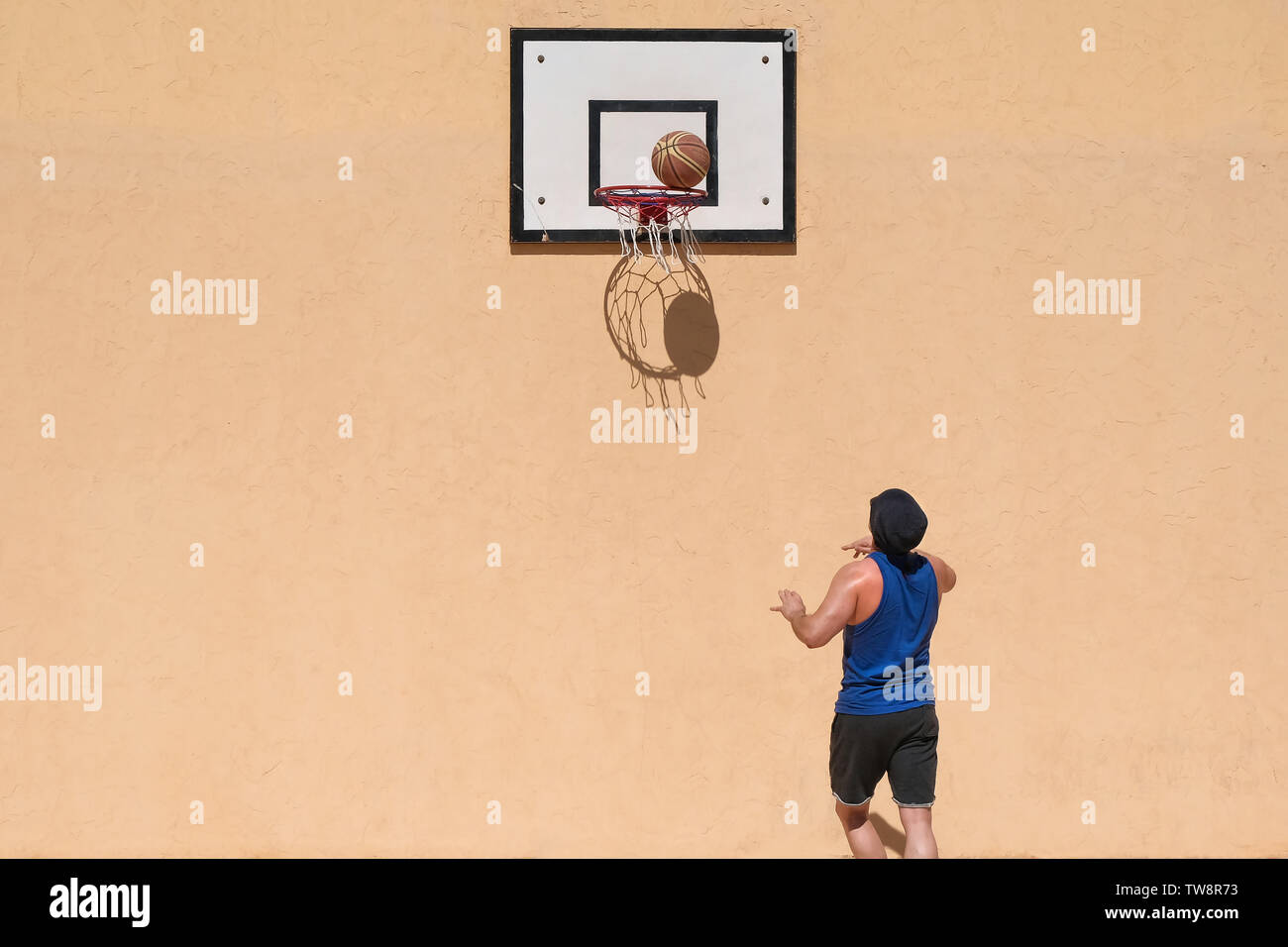 Un homme jouant au basket-ball sur son propre. La balle et le bénéfice net de créer des ombres sur le mur jaune Banque D'Images