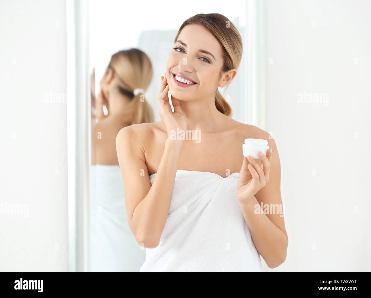 Young woman applying crème visage dans la salle de bains Banque D'Images