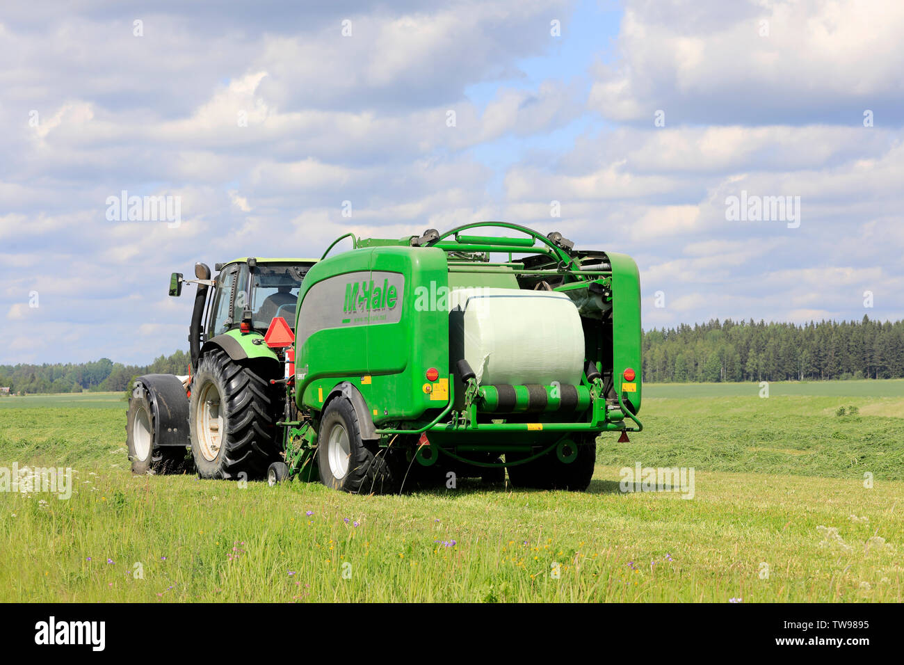 Salo, Finlande. Le 15 juin 2019. Tracteur Deutz-Fahr et McHale 3 plus l'ensilage en balles en plastique vert feuille dans champ de foin sur une journée ensoleillée d'été. Banque D'Images