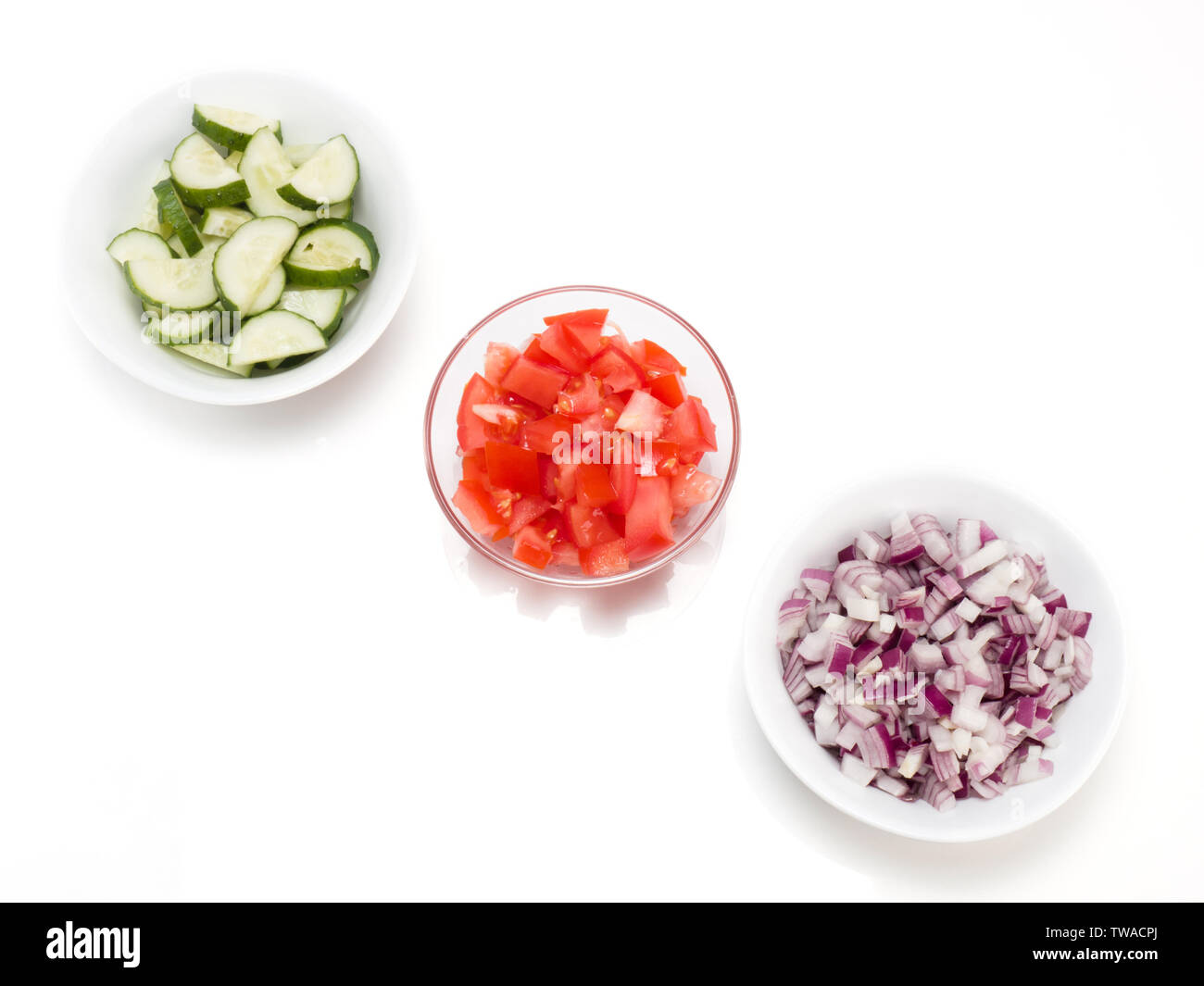 Tranches de tomate dans un bol transparent, oignons rouges et les concombres dans un bol blanc sur fond blanc Banque D'Images