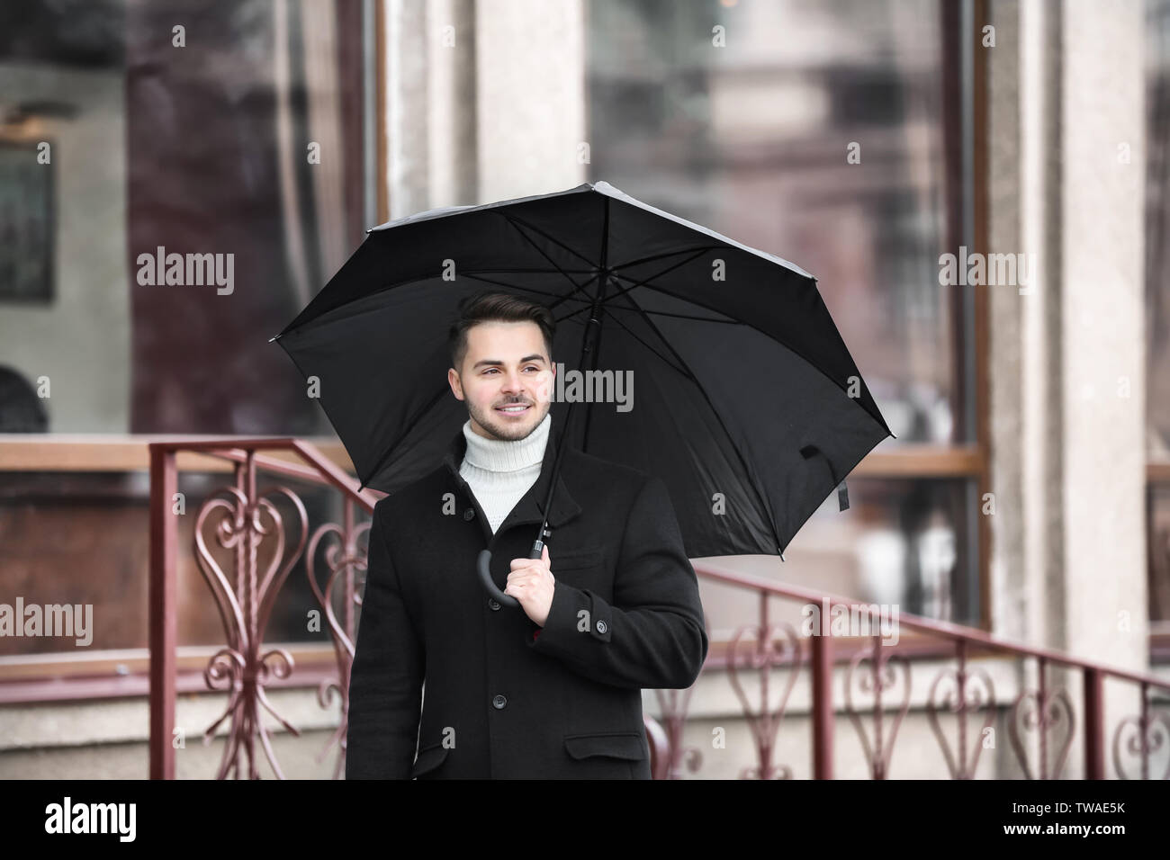 Jeune homme dans des vêtements chauds avec un parapluie en plein air Banque D'Images