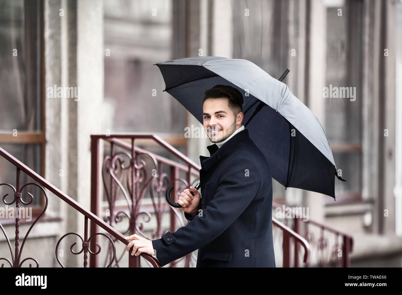 Jeune homme dans des vêtements chauds avec un parapluie en plein air Banque D'Images