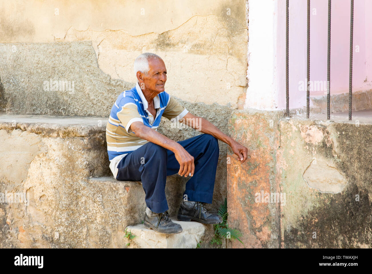 Un vieil homme cubain avoir une cigarette assis sur des pas dans la rue à Trinidad, Cuba. Banque D'Images