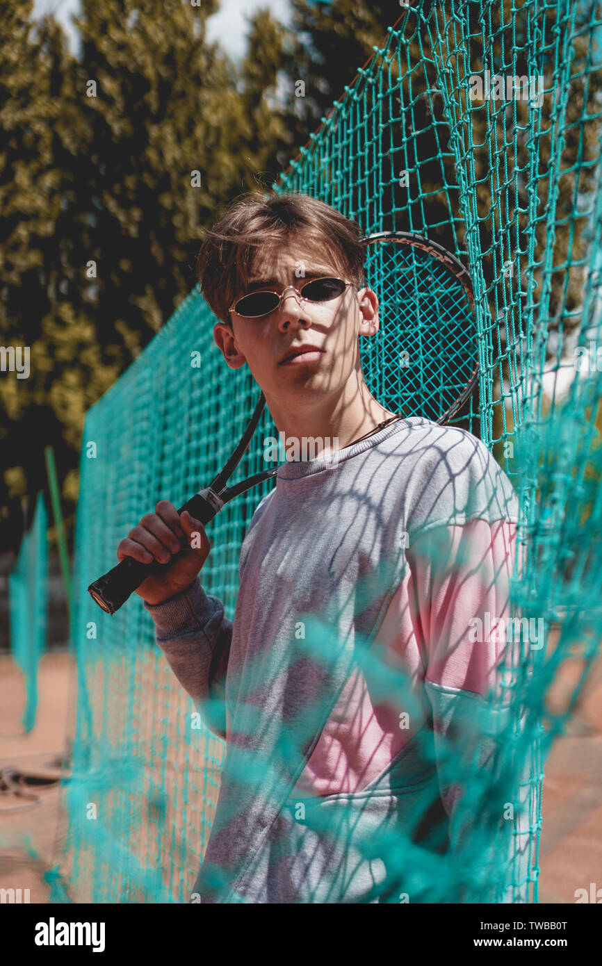 Jeune homme à l'extérieur d'un court de tennis dans un style élégant des  perspectives urbaines et des lunettes de soleil. Le mec est titulaire d'une  raquette de tennis Photo Stock - Alamy