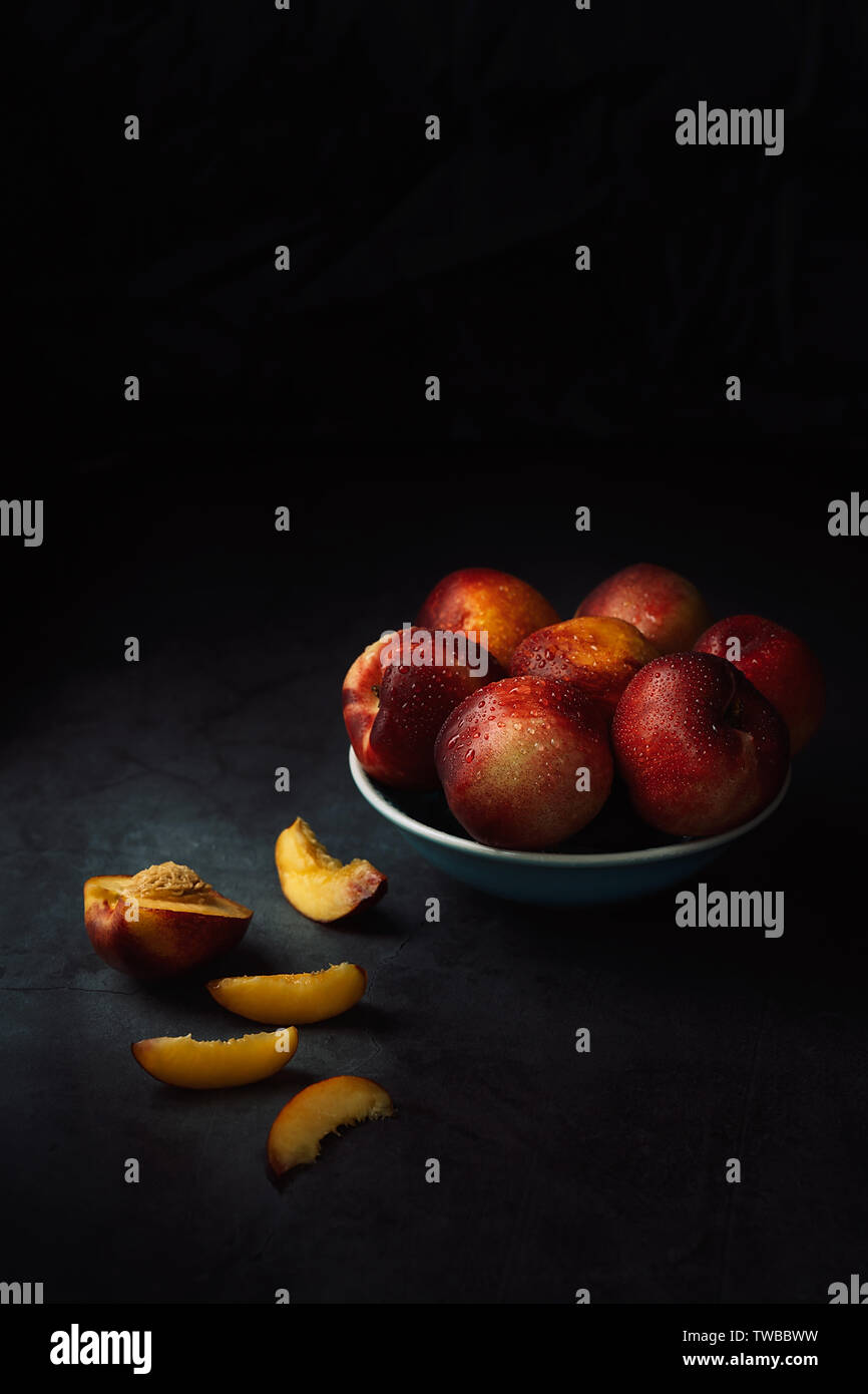 Still Life of fresh delicious sweet nectarines avec des gouttelettes d'eau dans un bol sur fond sombre. Clé faible. Banque D'Images