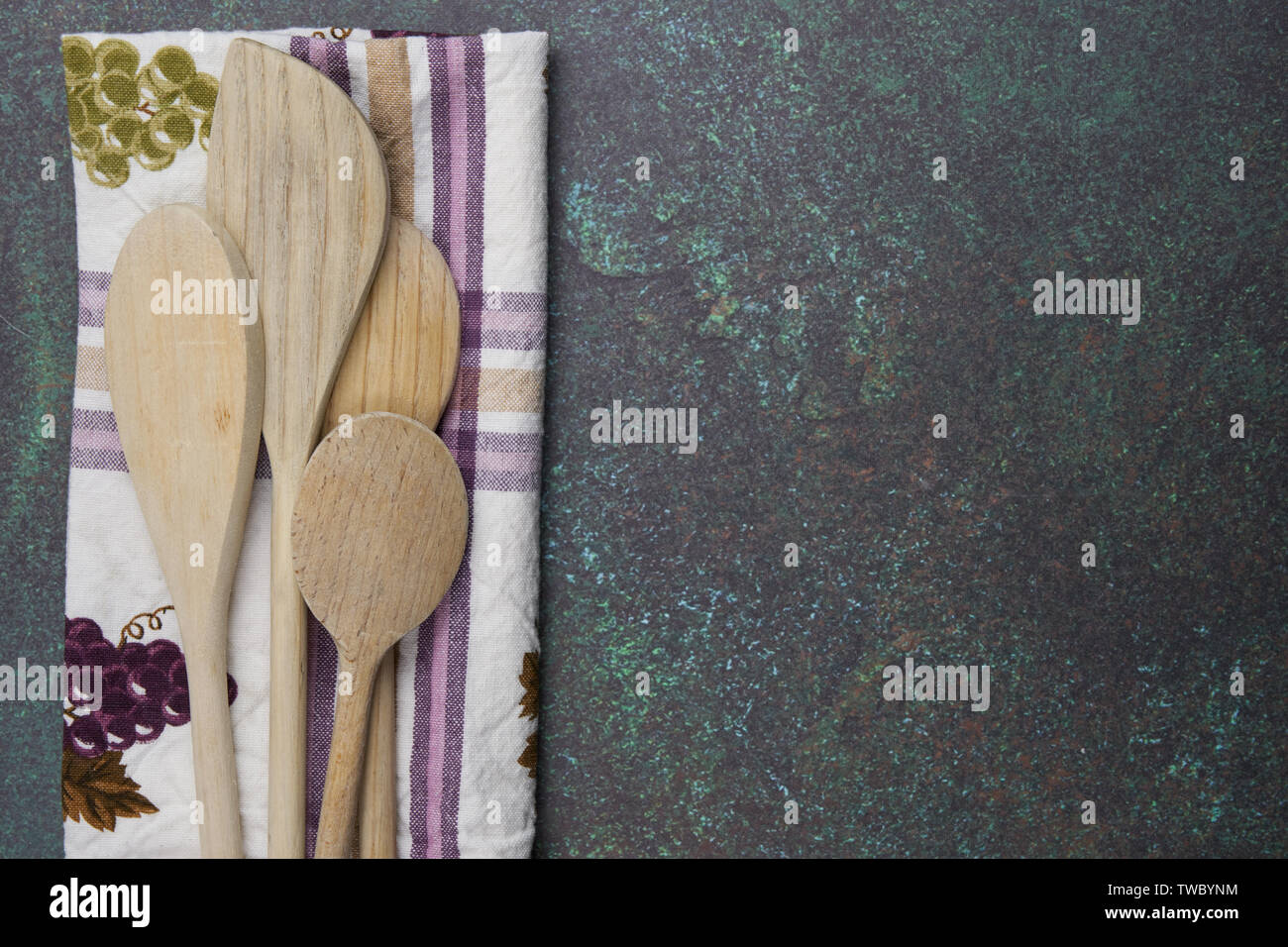 Quatre cuillères en bois avec un vert et violet à motifs à carreaux et les raisins sur une serviette de cuisine comptoir vert bleu Banque D'Images