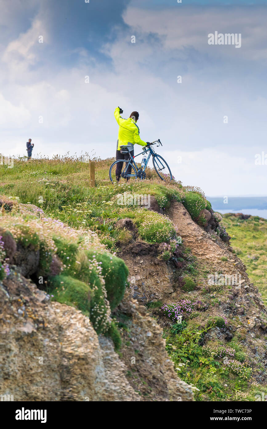 Un cycliste se tenant sur sa bicyclette et en tenant un téléphone mobile avec son selfies sur le bord des falaises sur la côte nord des Cornouailles. Banque D'Images Un cycliste se tenant sur sa bicyclette et en tenant un téléphone mobile avec son selfies sur le bord des falaises sur la côte nord des Cornouailles. Banque D'Images