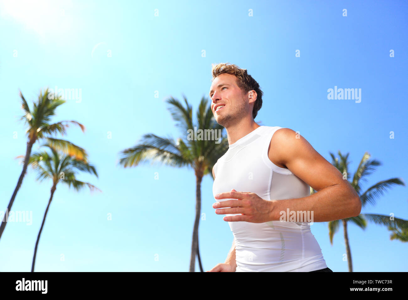 Sport homme d'exécution. Jogging runner athlète masculin en compression t-shirt haut formation sur les palmiers beach. Monter beau mâle modèle de remise en forme seul jogging pour formation de marathon. L'homme dans la vingtaine. Banque D'Images