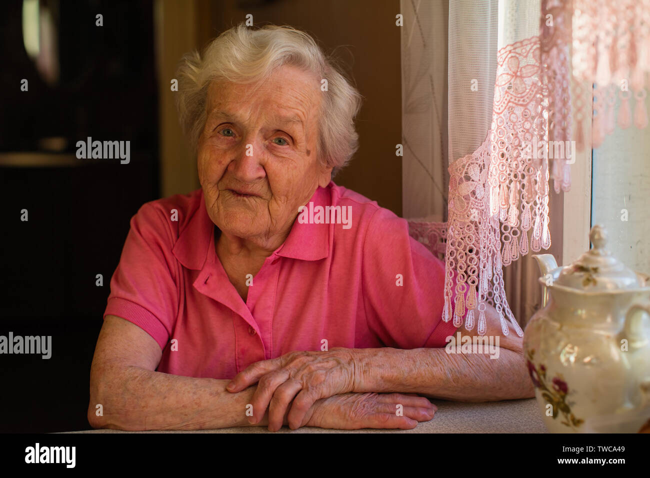 Portrait d'une vieille femme en habits rouges assis à la table. Banque D'Images