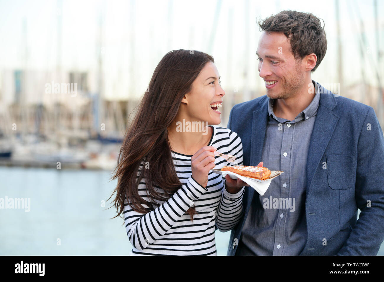 Couple heureux touristes de manger des gaufres, le vieux port de Barcelone, Port Vell, Catalogne, Espagne. L'homme et de la femme romantique rire s'amuser en plein air sur les voyages en Europe. Couple multiracial. Banque D'Images