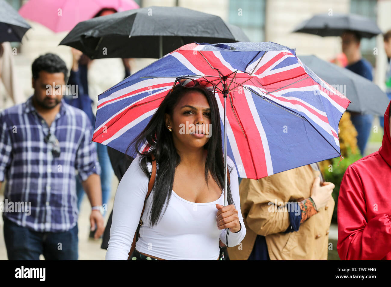 Les refuges d'une femme de la pluie sous un parapluie Union Jack au cours de l'averse lourde à Londres Banque D'Images
