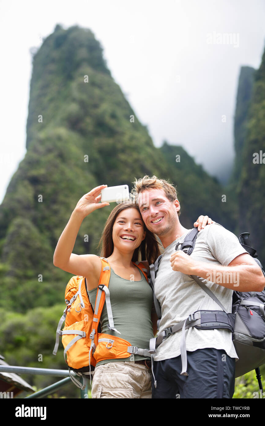 Couple taking self portrait selfies randonnées sur Hawaii en activité en plein air. La femme et l'homme hiker taking photo avec smart phone appareil photo. Style de vie sain de l'IAO Valley State Park, Wailuku, Maui, États-Unis. Banque D'Images