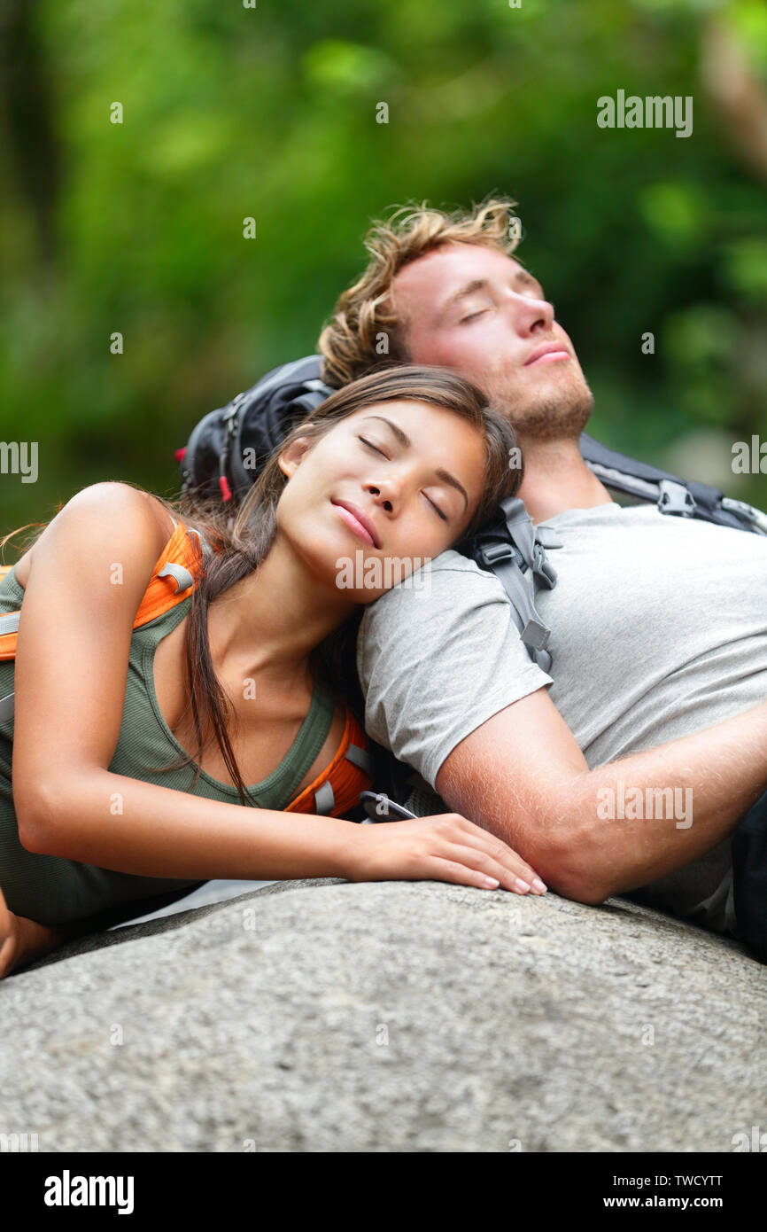 Les amateurs de randonnée couple relaxing dormir dans la nature. Essayé les randonneurs se reposer allongé à l'extérieur prenant une pause de la randonnée. Young Asian Woman and Caucasian man. Banque D'Images