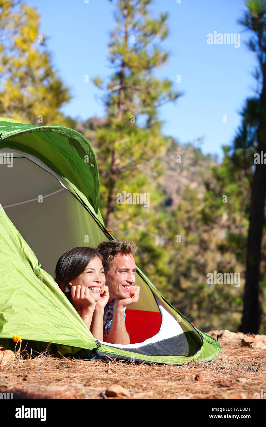 Couple camping en tente à la romantique à voir en forêt. Les campeurs smiling happy en plein air dans la forêt. Couple multiracial relaxant après activité de plein air. Asian Woman, man. Banque D'Images
