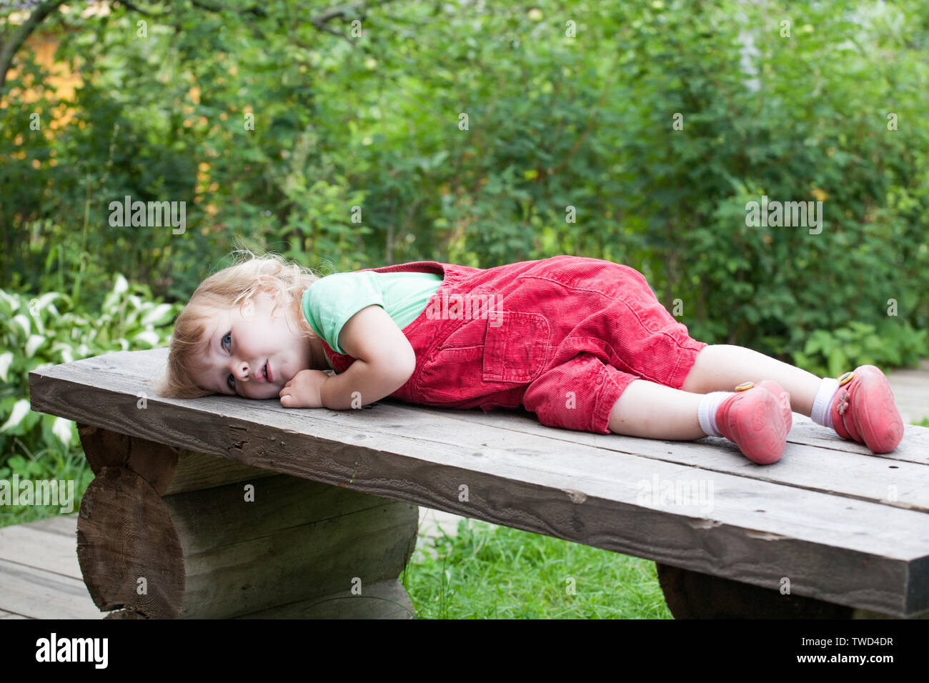Petit enfant pensive caucasian girl lying on outdoor banc en bois Banque D'Images