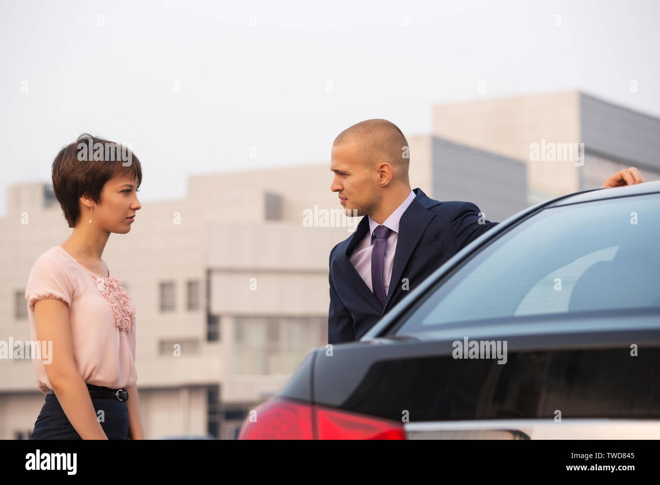 Mode jeune couple en conflit à parler à côté d'une voiture on city street élégant homme portant costume bleu foncé et d'une femme en blouse rose et noir sk Banque D'Images