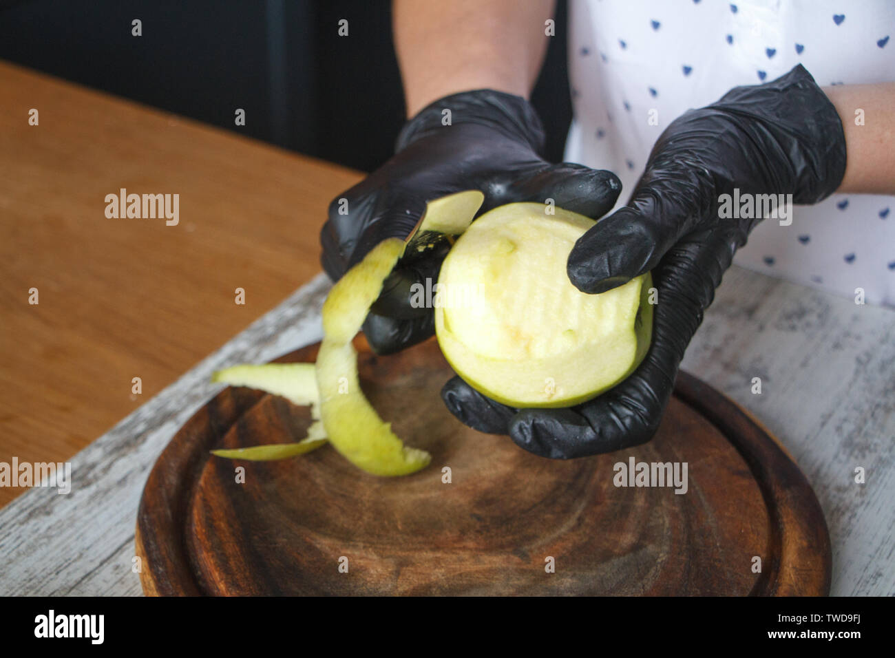 Femmes en noir gants peel off une pomme verte sur une planche en bois, selective focus, copyspace Banque D'Images