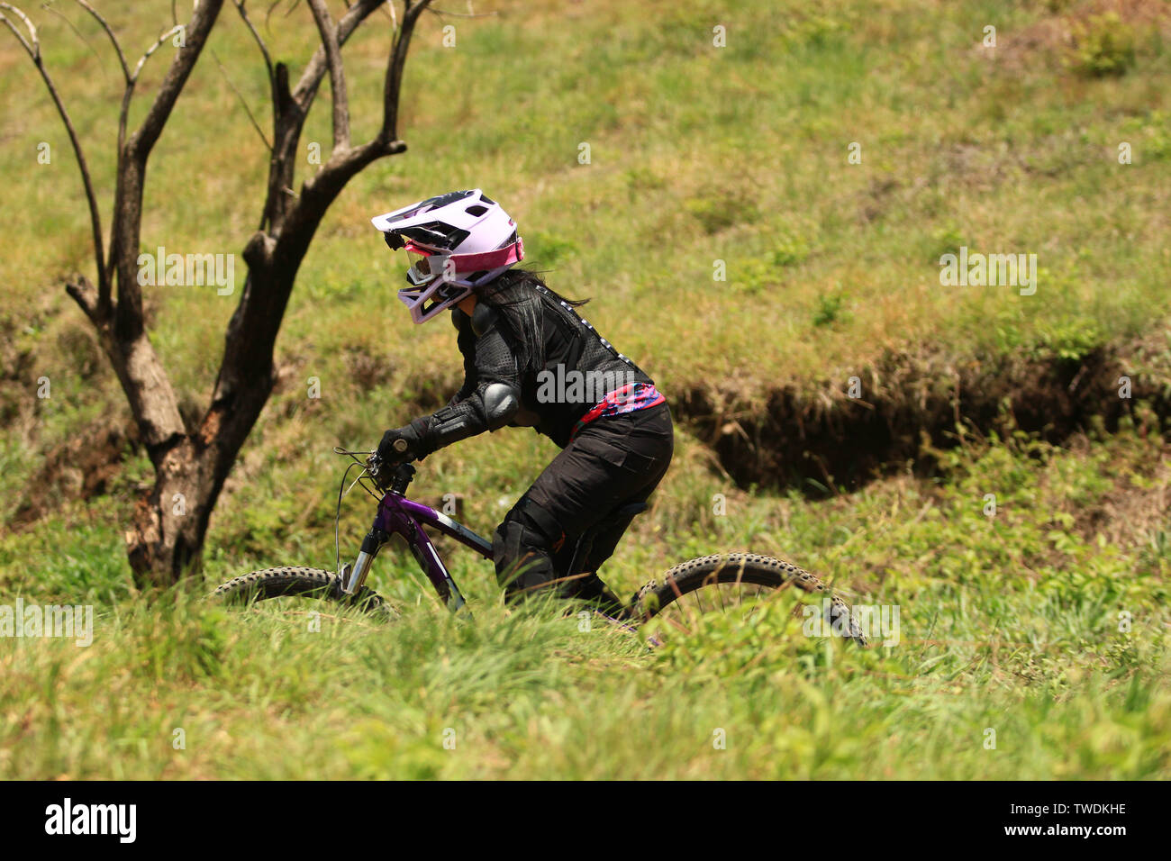 Un cycliste féminin portant un casque intégral équitation son vélo dans un champ d'herbe Banque D'Images