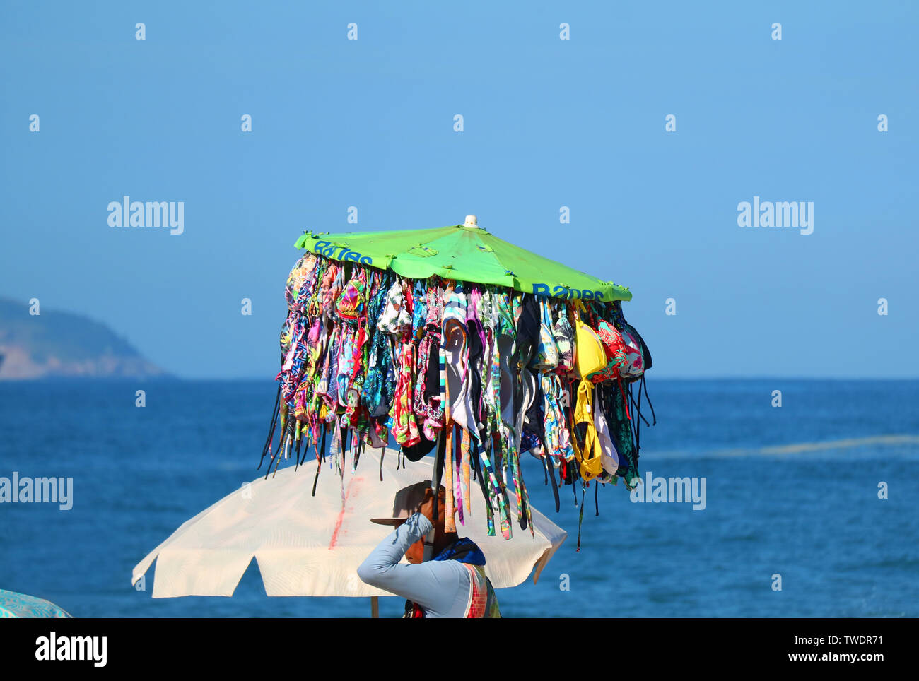 Maillot de bain' vendeur transportant beaucoup de bikinis marchant le long de la plage avec l'océan en arrière-plan Banque D'Images