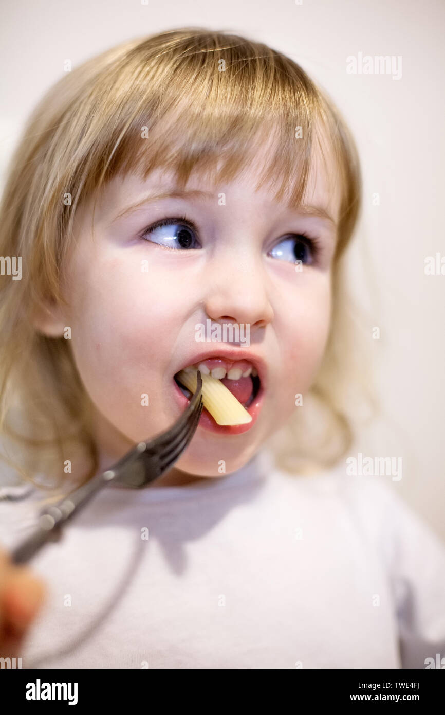 Visage gros plan de little white girl eating pasta par une fourche Banque D'Images