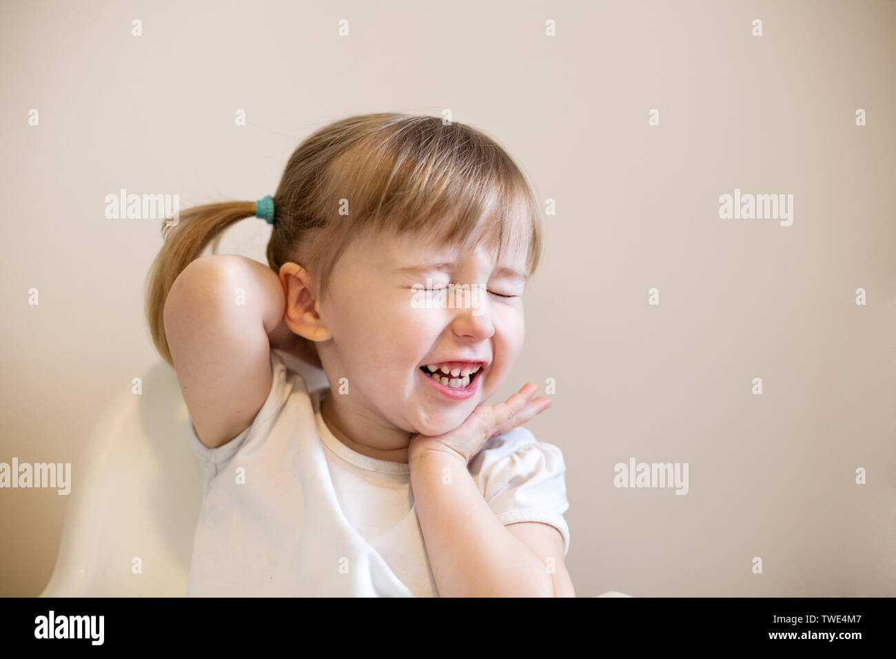 Peu de rire kid Caucasian girl aux yeux clos mignon visage gros plan sur fond uni Banque D'Images