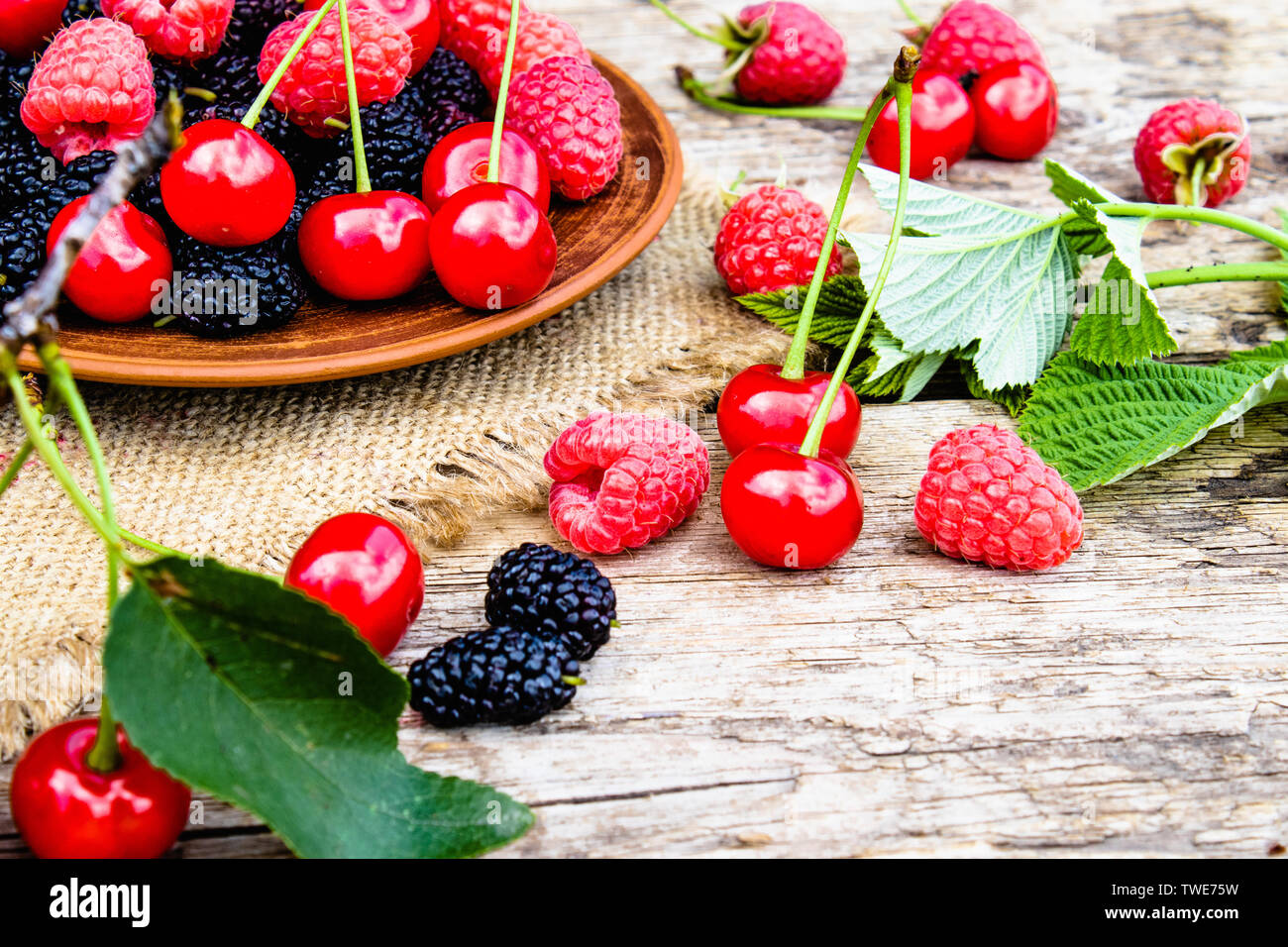 Fruits des framboises, cerises, mûres dans un bol sur fond de bois et de toile. Close-up Banque D'Images