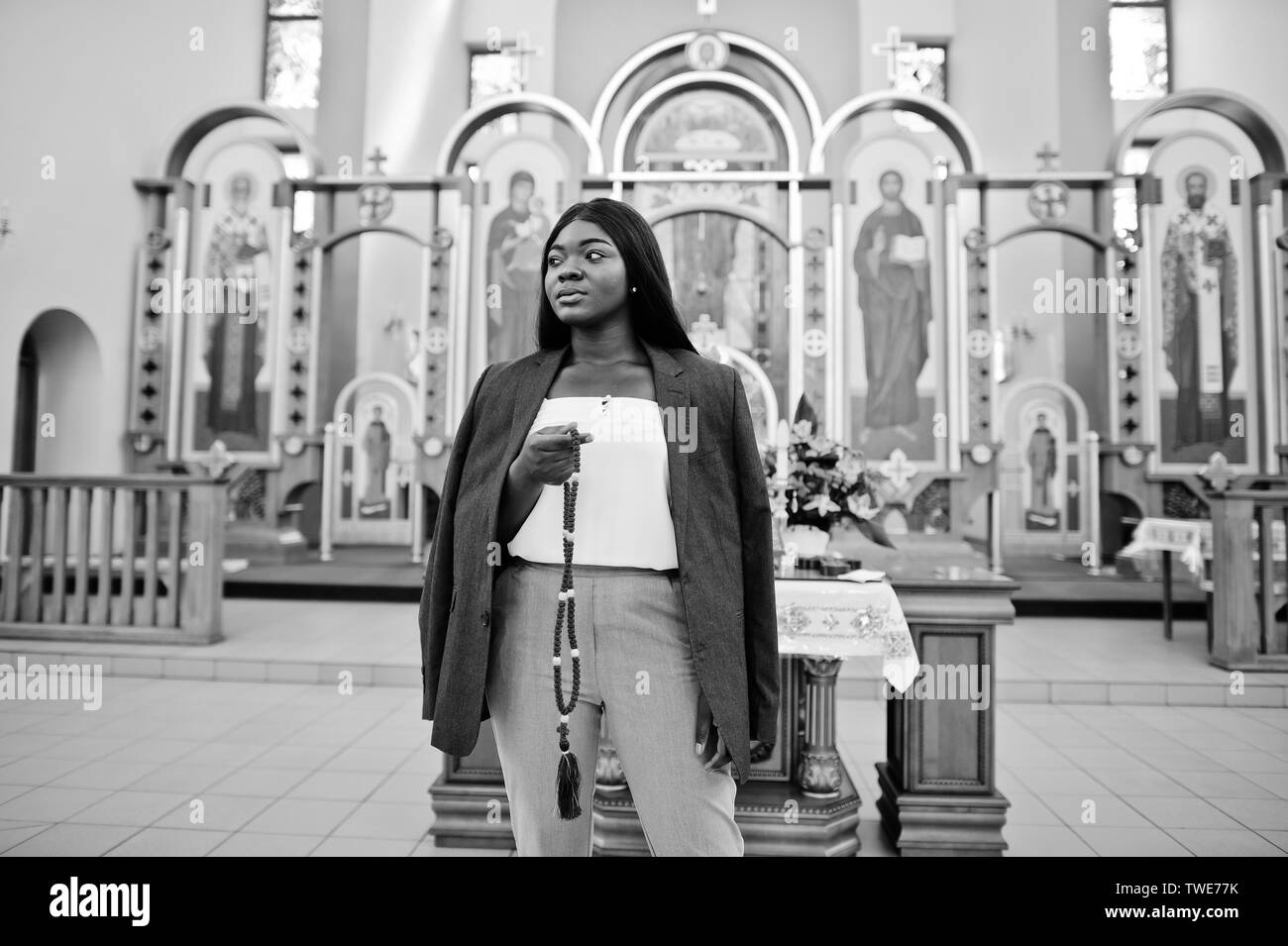African American Woman priant dans l'église. Croyants médite dans la cathédrale et temps spirituel de la prière. Afro girl avec rosaire sur les mains. Banque D'Images