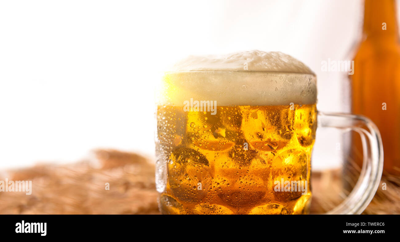 Cruche pleine de bière avec de la mousse et derrière la bouteille sur la table en bois décoré avec des épis d'orge avec fond blanc. Composition horizontale. Vue de face. Banque D'Images