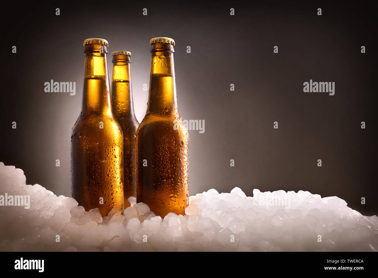Trois bouteilles de bière plein sur de la glace concassée et dark background . Composition horizontale. Vue de face. Banque D'Images