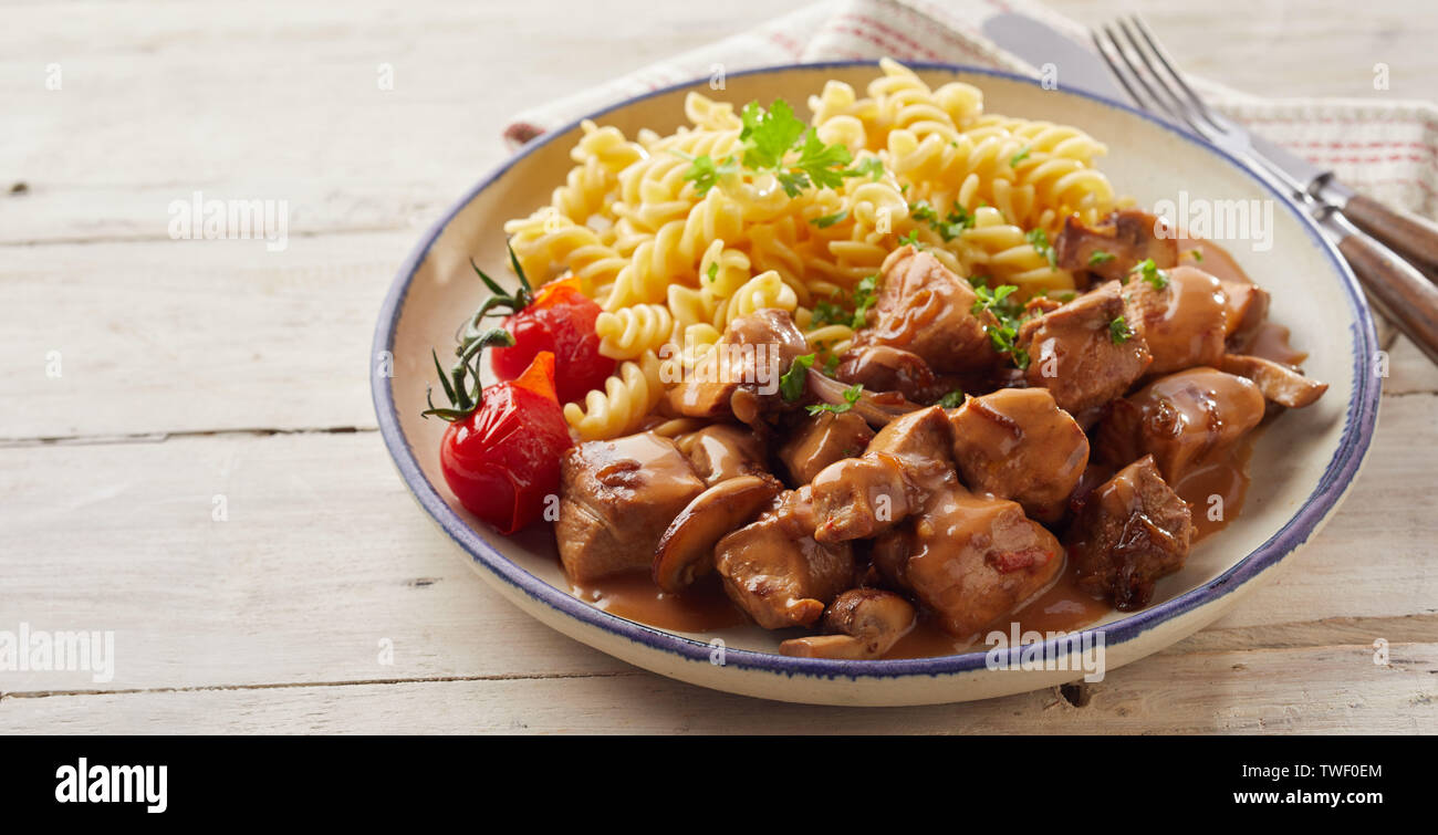 Spiral plat de pâtes fusilli avec dés de porc et les tomates dans un bol à côté de fourchette et couteau sur table en bois Banque D'Images