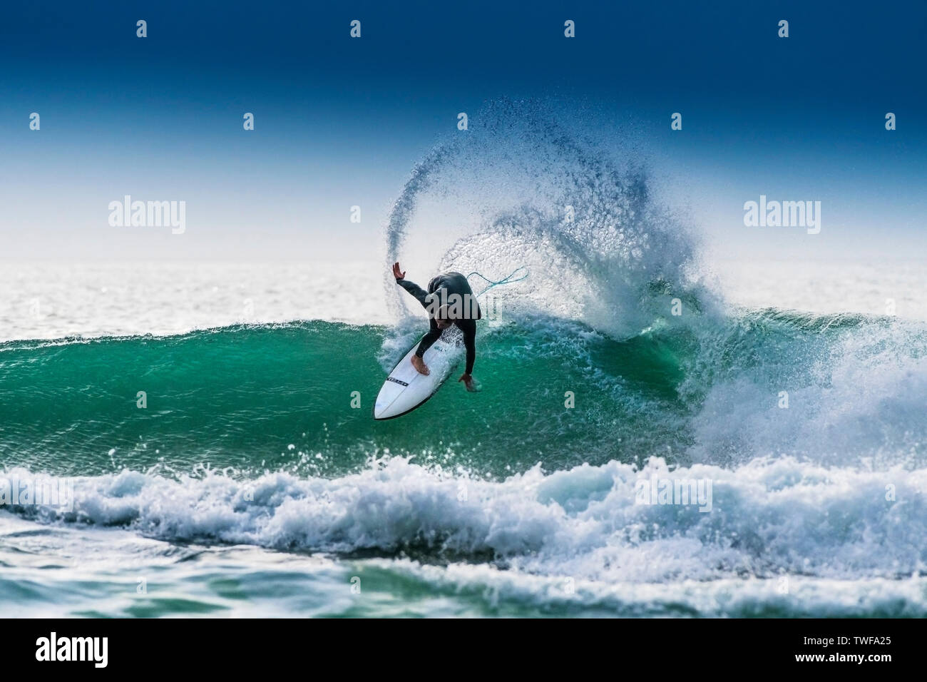 Un surfeur équitation un surf sur la crête d'une vague de couleur jade dans Fistral Newquay à à Cornwall. Banque D'Images