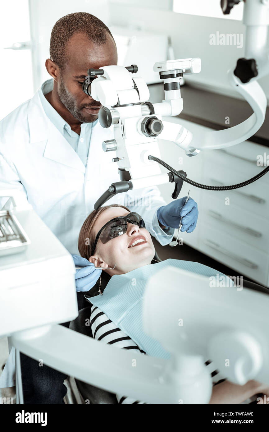 À l'aide de la machine. Smiling woman in lunettes de protection situés sous l'appareil dentiste pendant qu'il la réalisation d'outils métalliques Banque D'Images