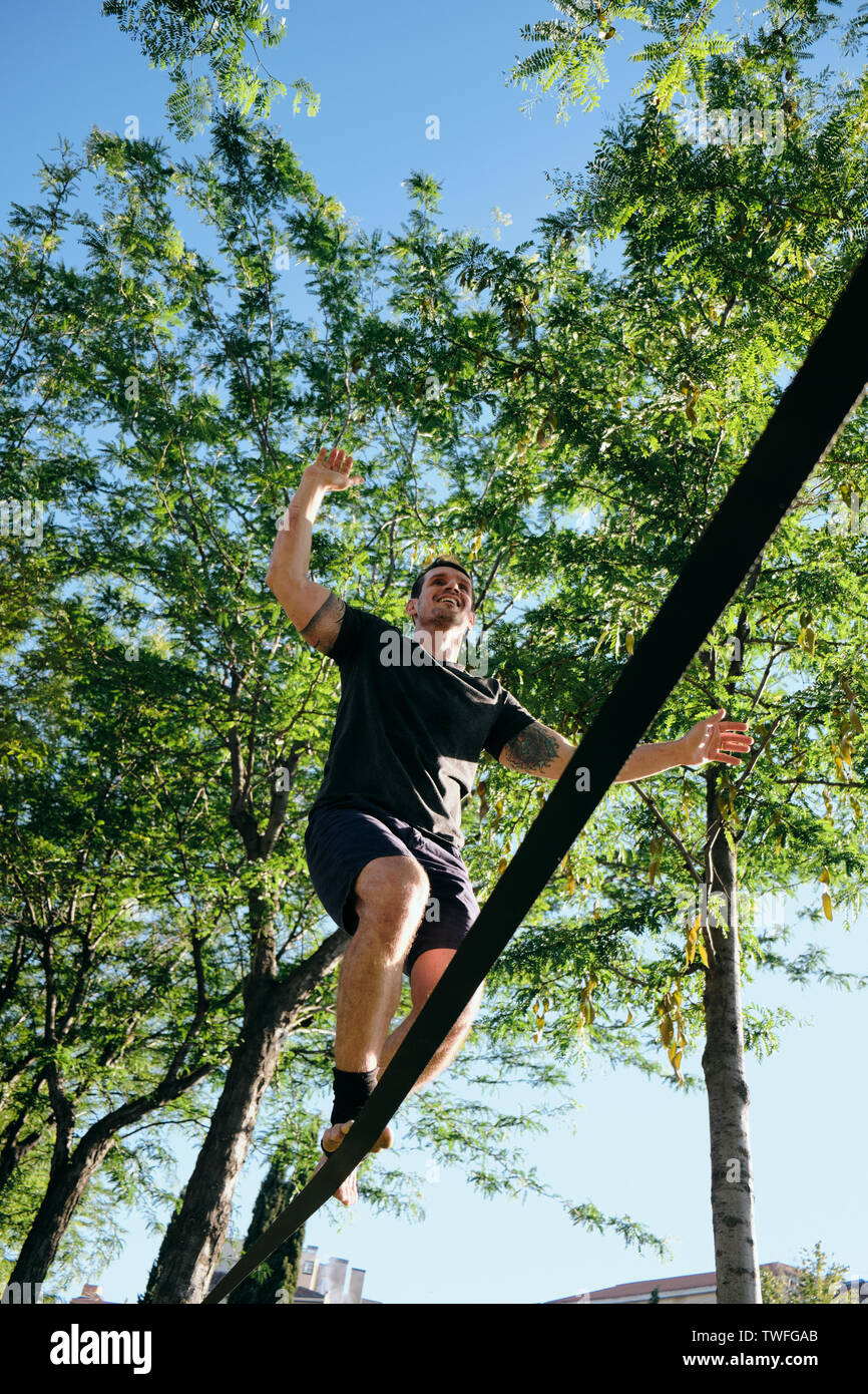 Mid adult man sauter et marcher sur la corde accroché dans les arbres, faire une routine de travail trickline à Madrid, Espagne. Banque D'Images
