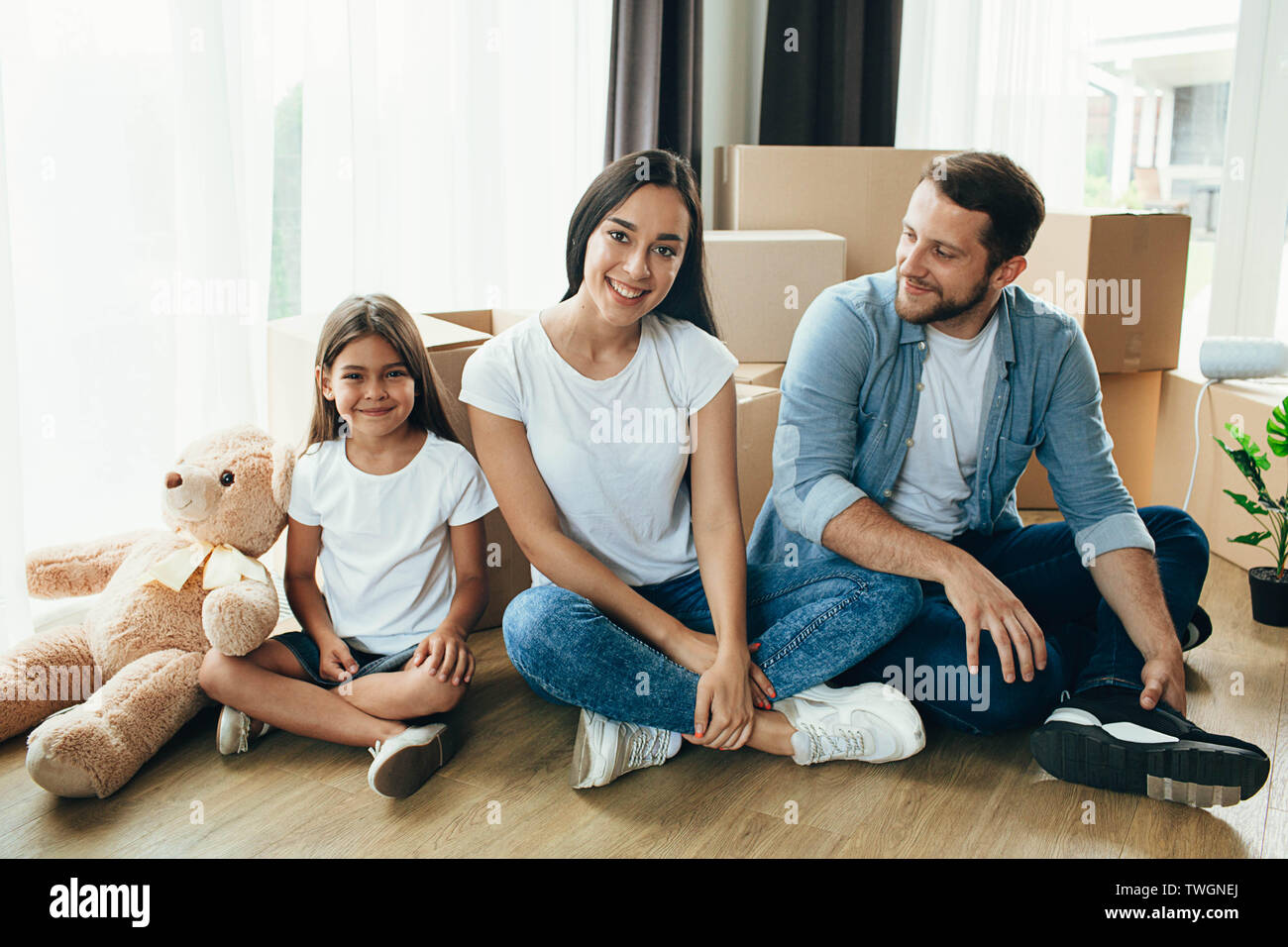 Jolie famille déménager. Couple avec enfant assis sur leur nouvel appartement avec de nombreux cartons Banque D'Images