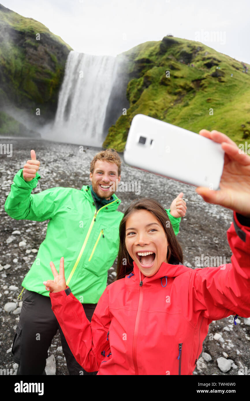 Couple selfies selfies funny photo smartphone de l'extérieur, dans la cascade de Skogafoss avant sur l'Islande. Visite de deux célèbres attractions touristiques et monuments de la nature islandaise paysage. Banque D'Images