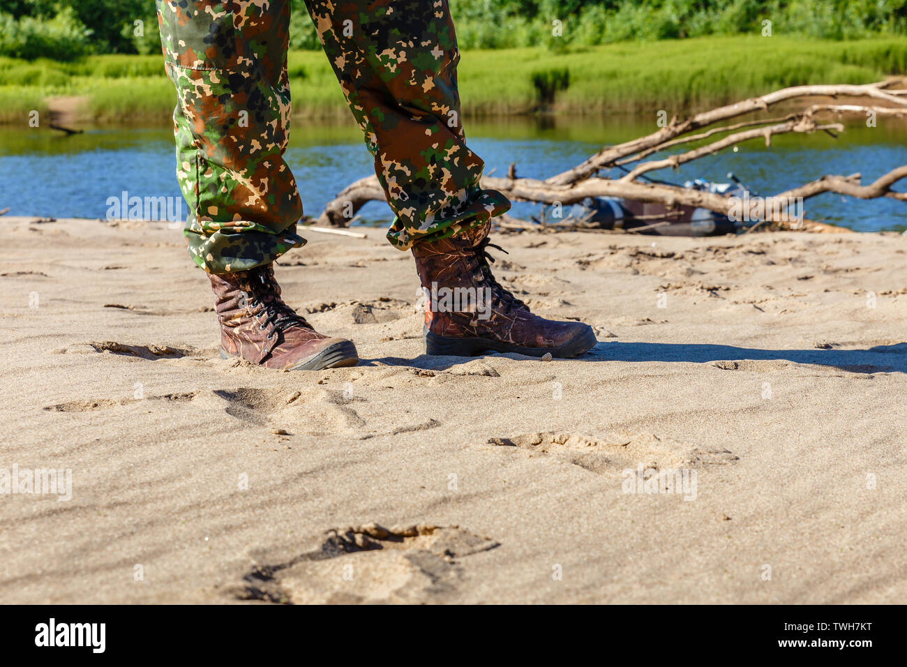 Les pieds des hommes en bottes et pantalon camouflage sur le sable au bord de la rivière Banque D'Images