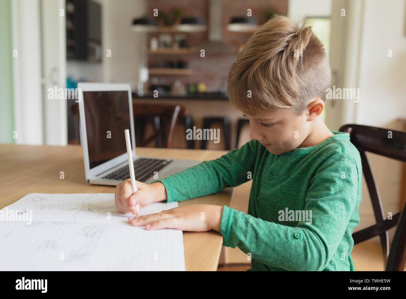 Cute boy doing homework at table à manger dans une maison confortable Banque D'Images