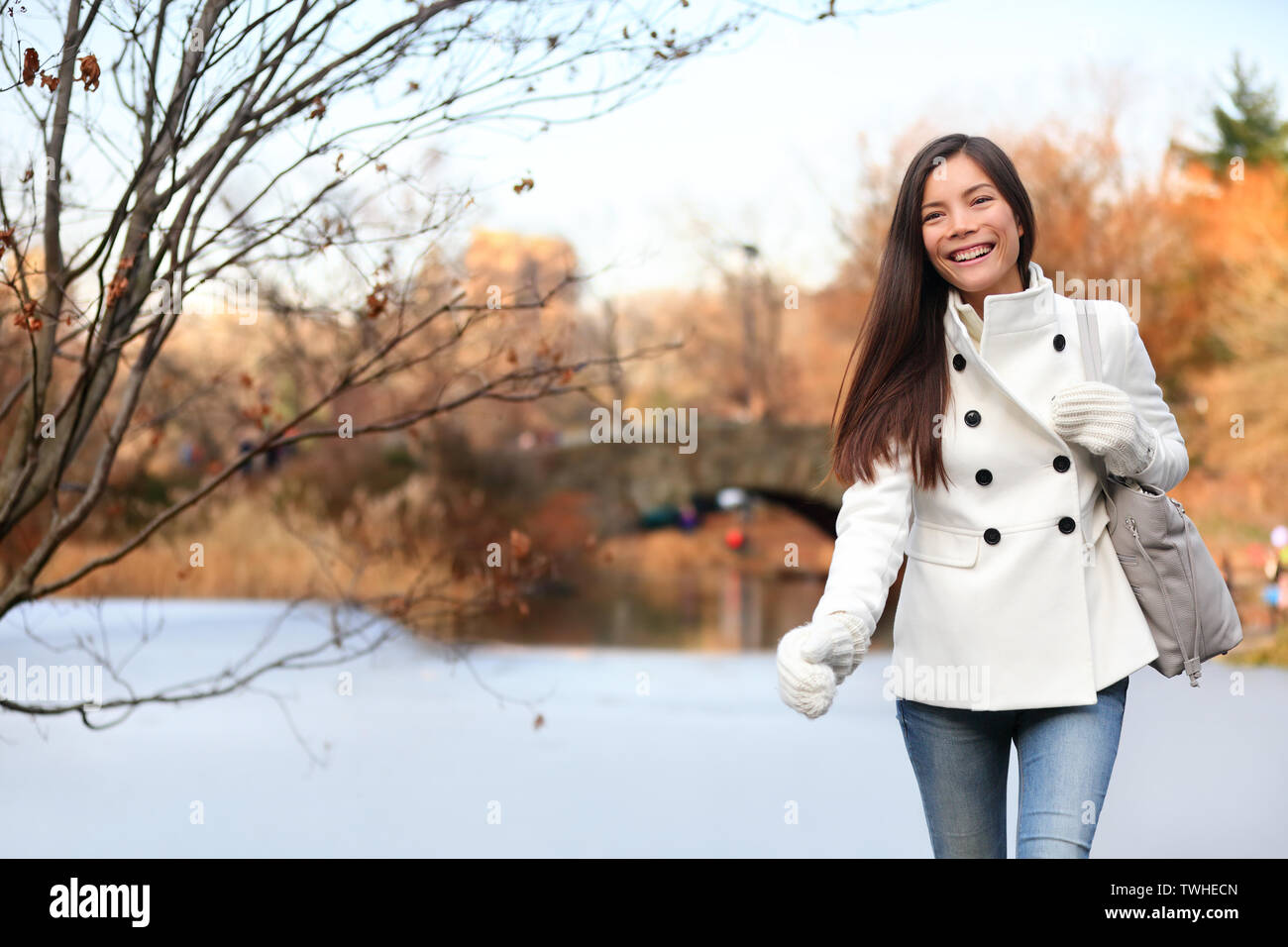 Woman walking heureux dans Central Park, New York City à la fin de l'automne au début de l'hiver avec patinoire en arrière-plan. Sourire candide fille multi-ethnique sur Manhattan, USA. Banque D'Images