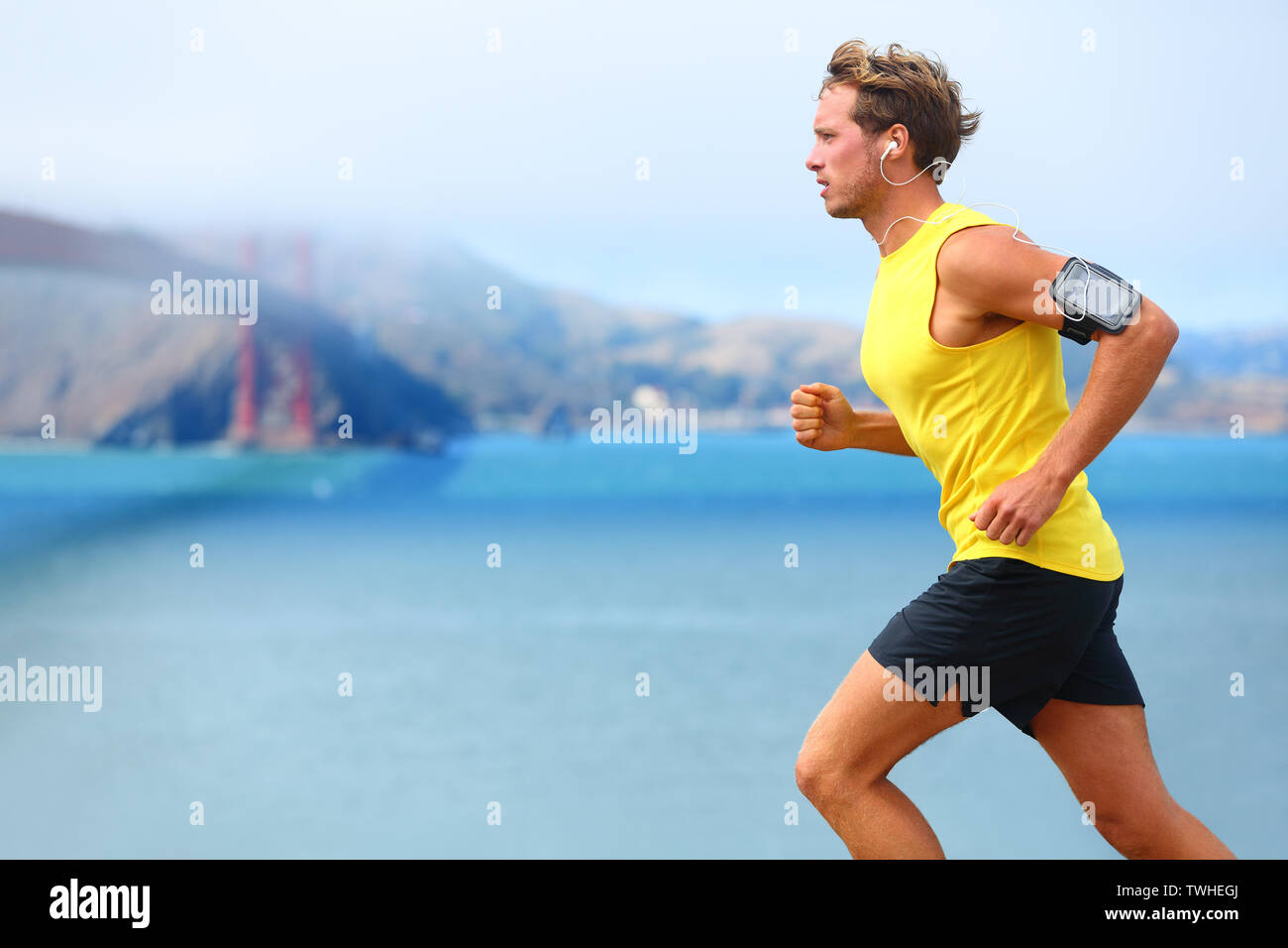 Athlète running man - hommes runner à San Francisco l'écoute de musique sur smartphone. Mettre en place sportive young man jogging par baie de San Francisco et le Golden Gate Bridge. Jogger avec formation brassard, smart phone Banque D'Images