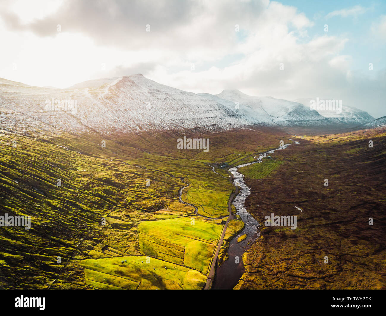 Des images aériennes d'une vallée des îles Féroé à Saksun pendant le coucher du soleil avec les montagnes neige-couvertes, une rivière, des nuages bas et des champs (îles Féroé) Banque D'Images